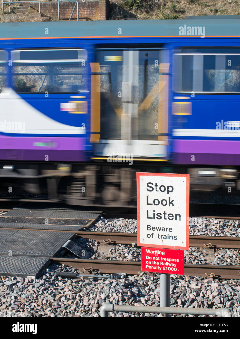 Velocità del treno sfocata passa ungated livello pedonale attraversamento su ferrovia, Durham costa North East England Regno Unito Foto Stock