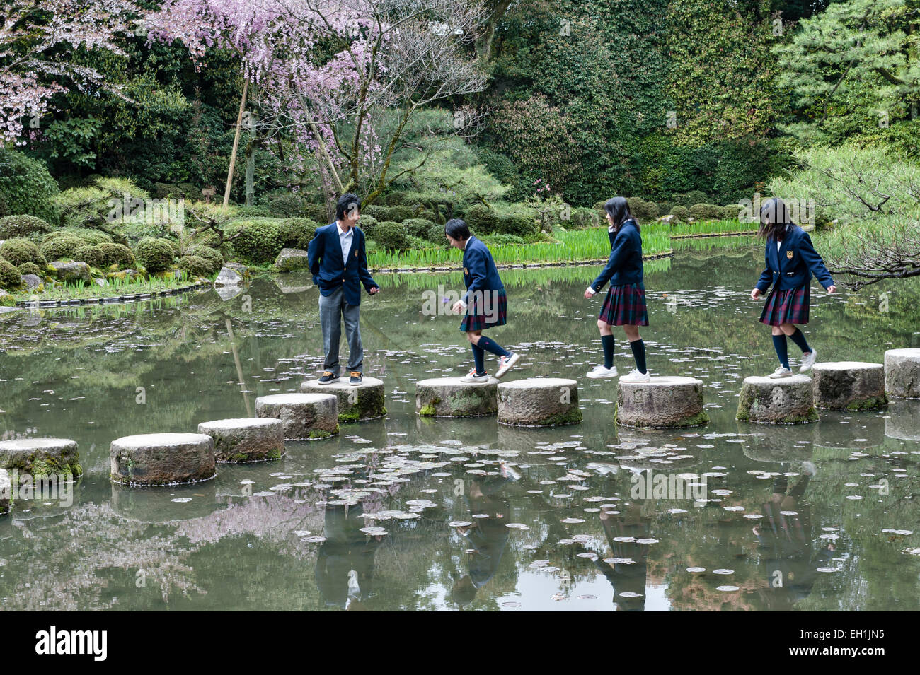 Scolari che attraversano le pietre di lancio attraverso il lago nei giardini 19c del Santuario Heian (Heian Jingu), un tempio shintoista a Kyoto, in Giappone Foto Stock
