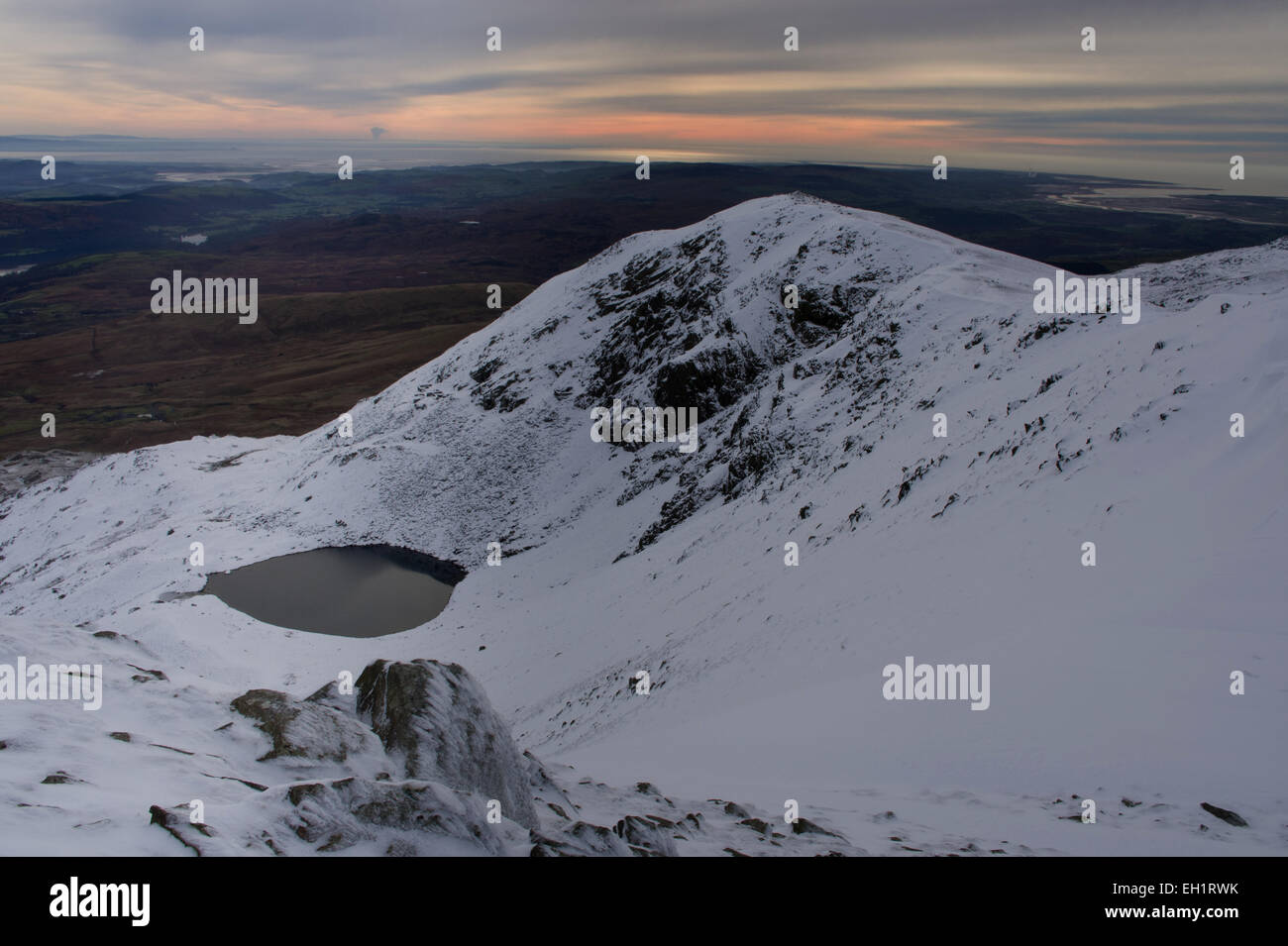 Escursionisti invernali sulla neve Dow falesia. Buck marrone Pike, cieco Tarn lattiginoso cielo invernale, snowy Dow Crag da Coniston Old Man Foto Stock