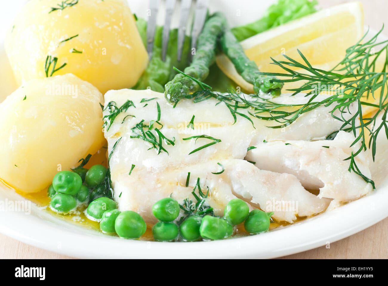 Merluzzo cotto con il burro fuso e aneto. Servito con patate e piselli verdi. Foto Stock