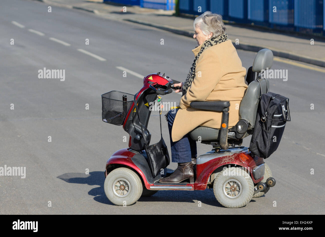 Mobilità scooter - signora anziana attraversare una strada in una mobilità scooter NEL REGNO UNITO. Senior donna disabilità scooter. Foto Stock