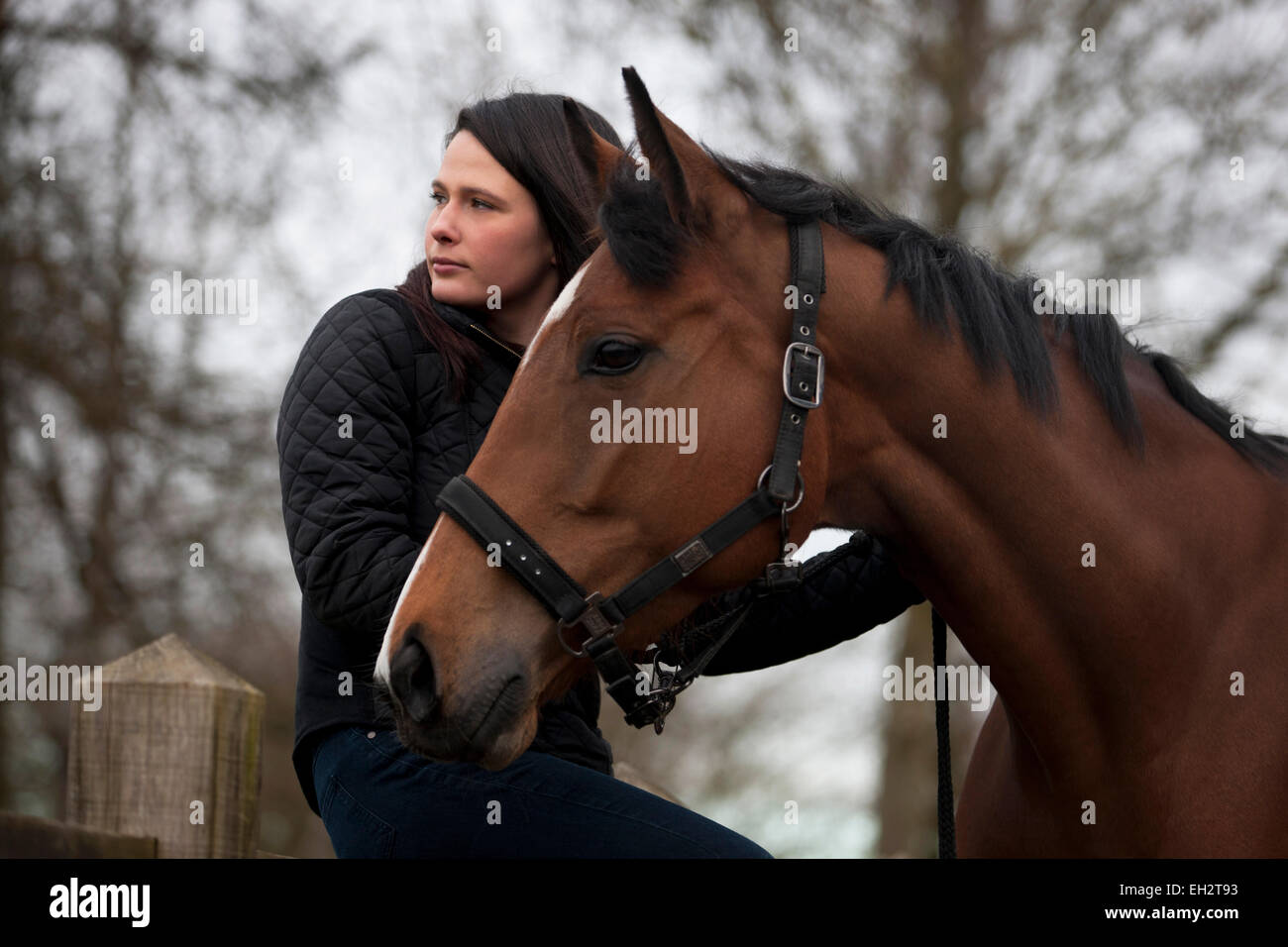 Una giovane donna seduta su un recinto, tenendo un cavallo Foto Stock