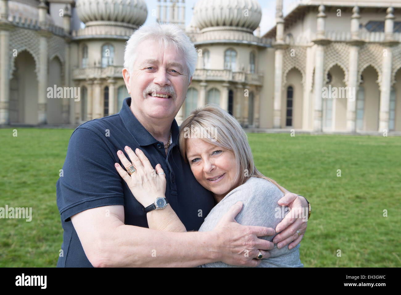 Una coppia di anziani coccolare e abbracciare mostra amore davanti al Brighton è punto di riferimento turistico il Royal Pavilion sull'erba Foto Stock