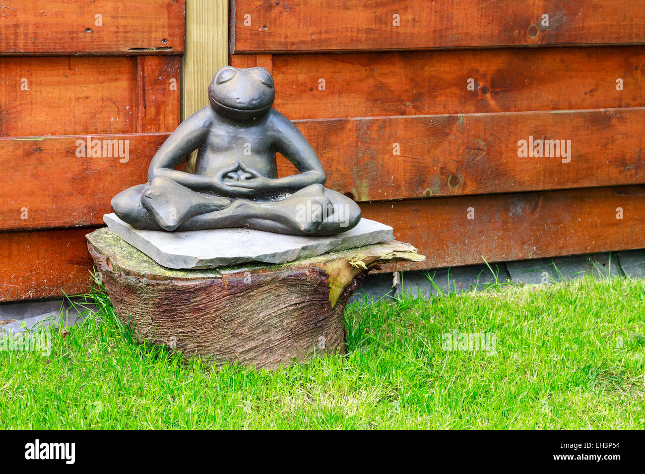 Il giardino di pietra a forma di rana meditando in un giardino seduto su un tronco di albero Foto Stock