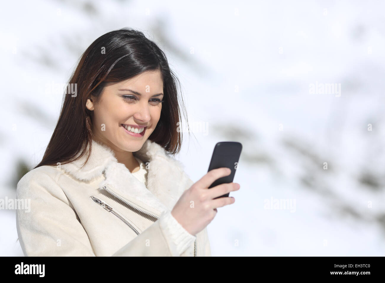 Donna che utilizza un telefono intelligente su vacanze invernali con una montagna innevata in background Foto Stock