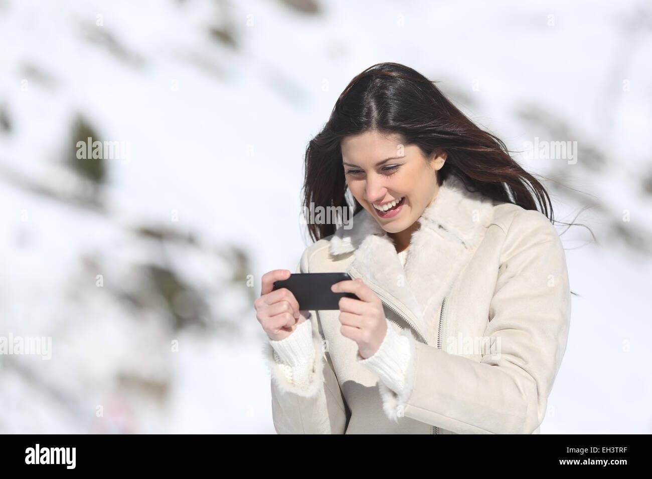 Donna felice i giochi in uno smart phone su vacanze invernali con una montagna innevata in background Foto Stock