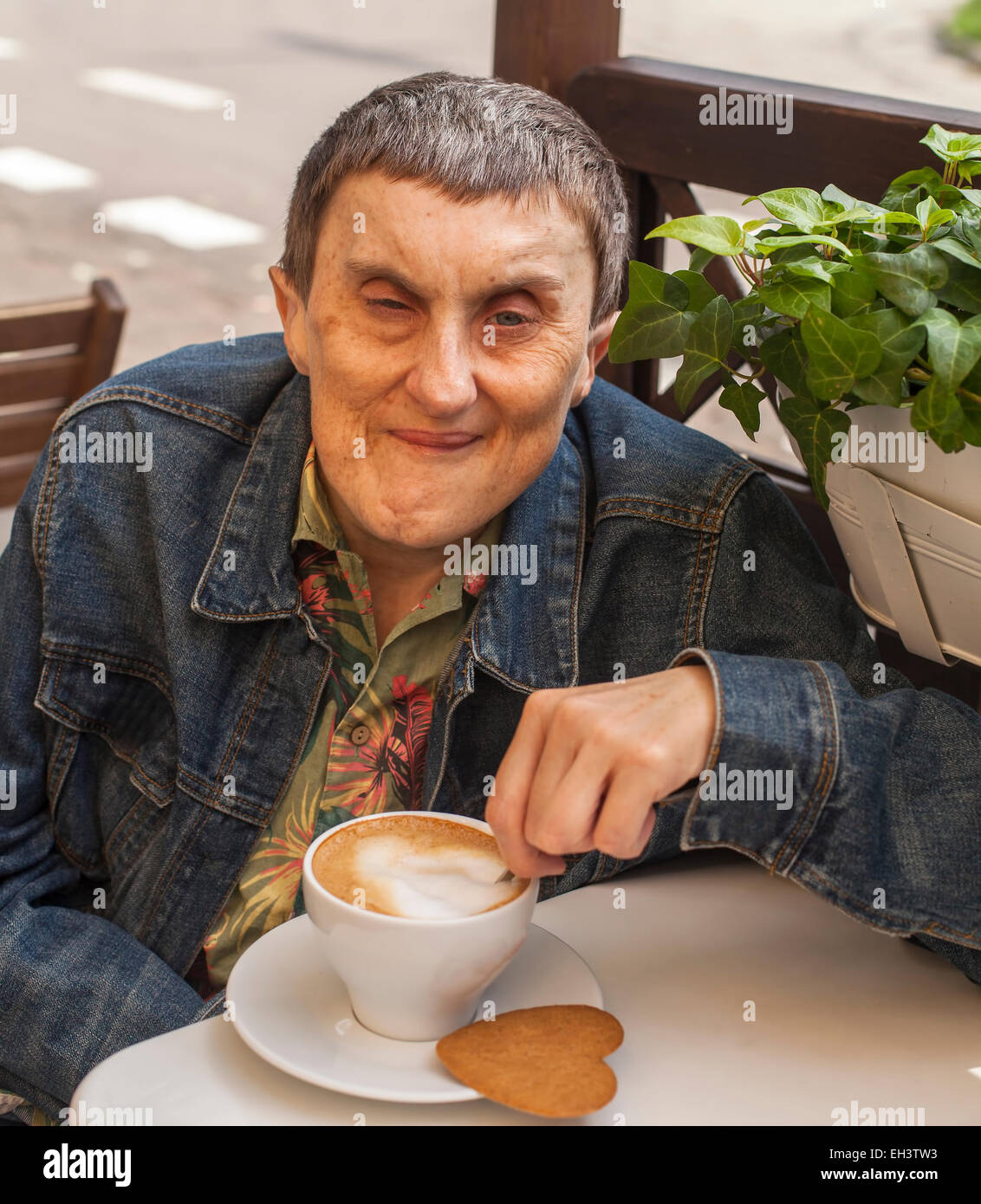 Disabilitato l'uomo con paralisi cerebrale seduti al cafe esterno con una tazza di caffè. Foto Stock
