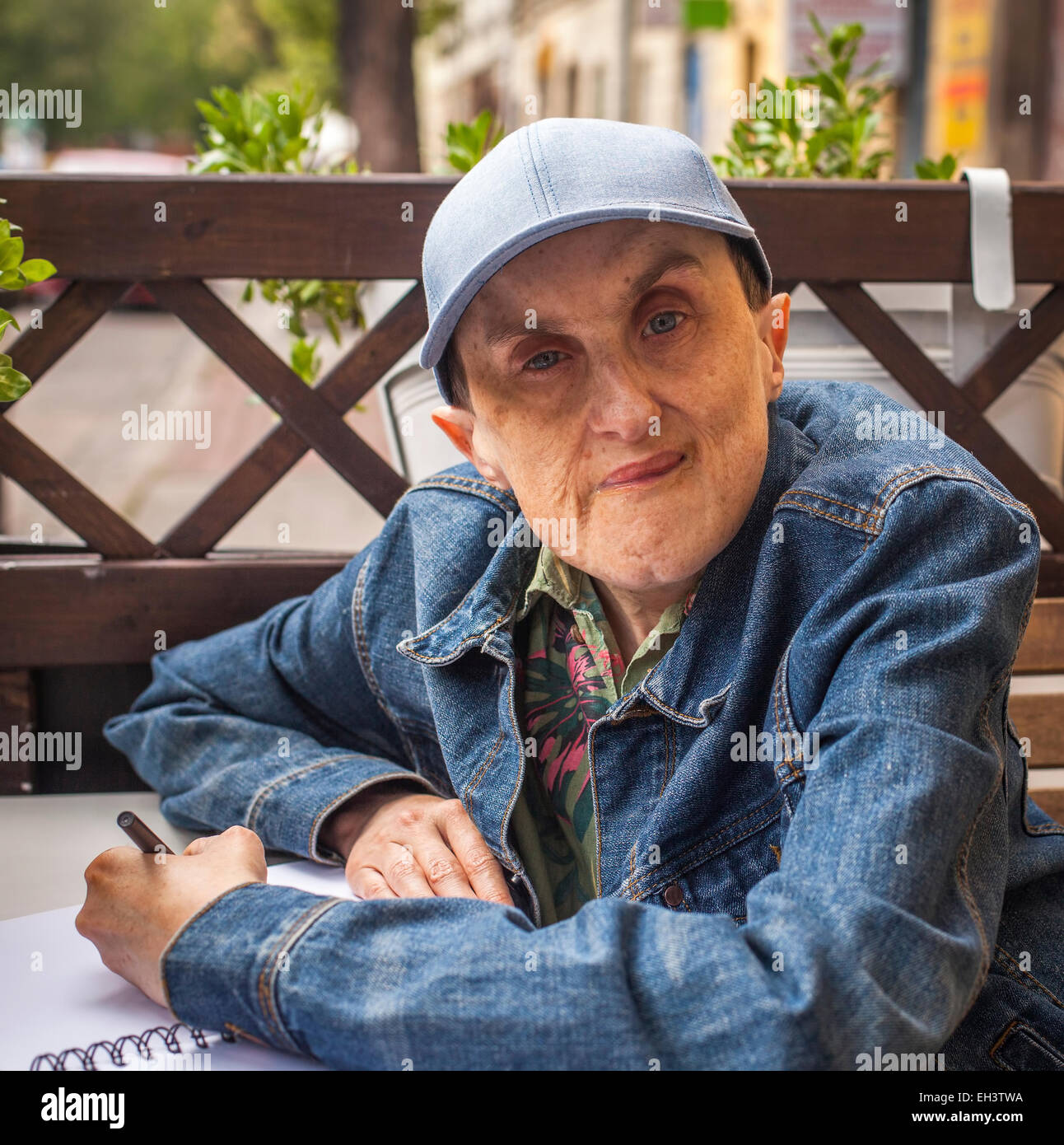 Disabilitato l'uomo con paralisi cerebrale seduta a outdoor cafe con un notebook e una matita. Foto Stock