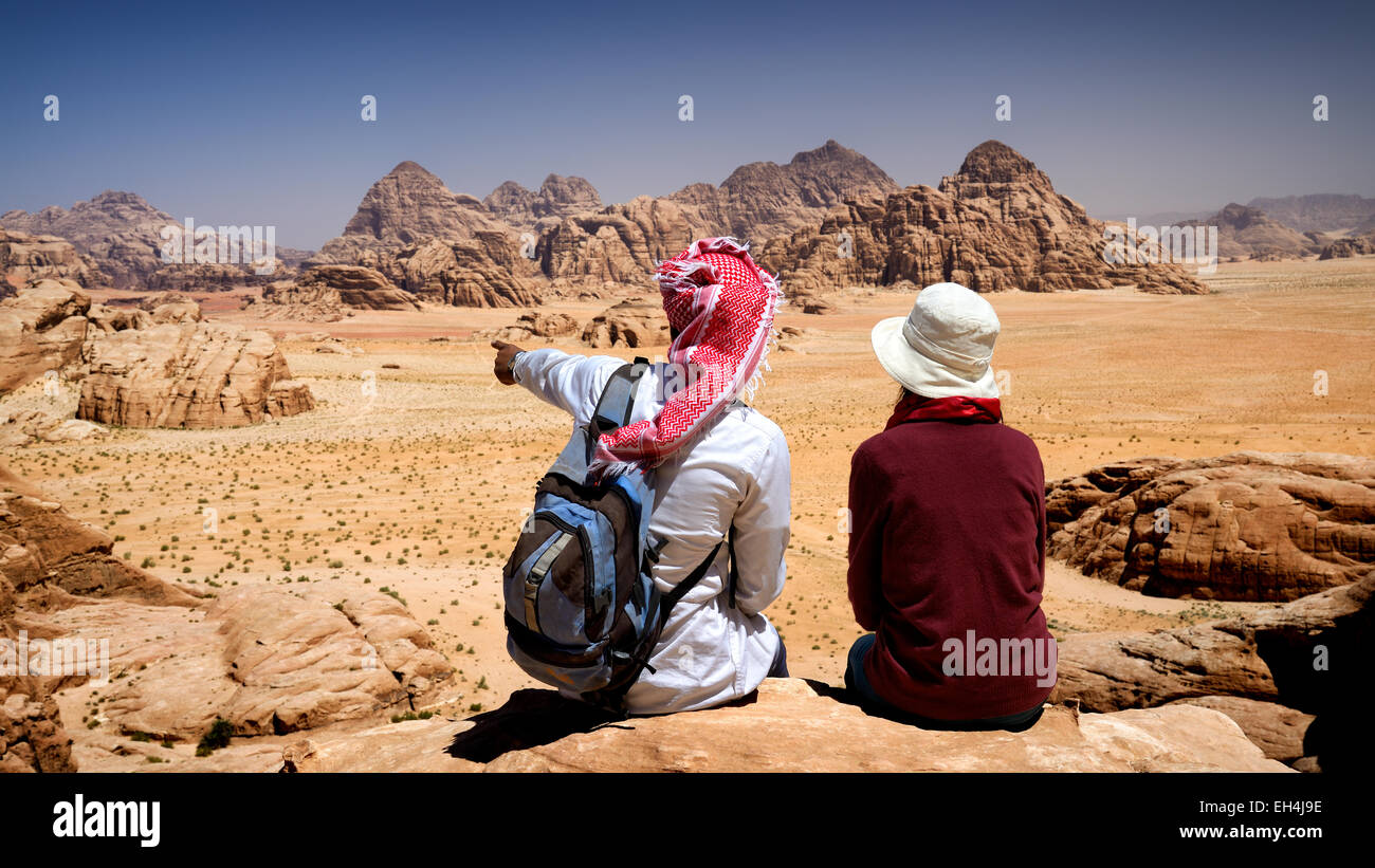 Giordania, Wadi Rum desert, area protetta elencati come patrimonio mondiale dall' UNESCO, turistici e locali guida beduino seduto su di una roccia, contemplando il paesaggio dal Monte Jebel Burdah Foto Stock