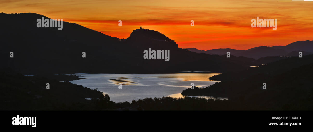 Spagna, Andalusia, Cadix, Zahara de la Sierra, lago ai piedi di una rupe su cui sorge una torre di avvistamento contro la luce al tramonto Foto Stock