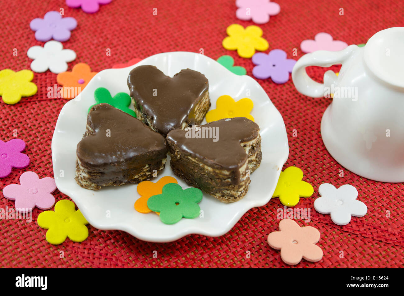 Al cioccolato a forma di cuore i cookie su una piastra decorato con fiori di carta su una tovaglia rosso Foto Stock