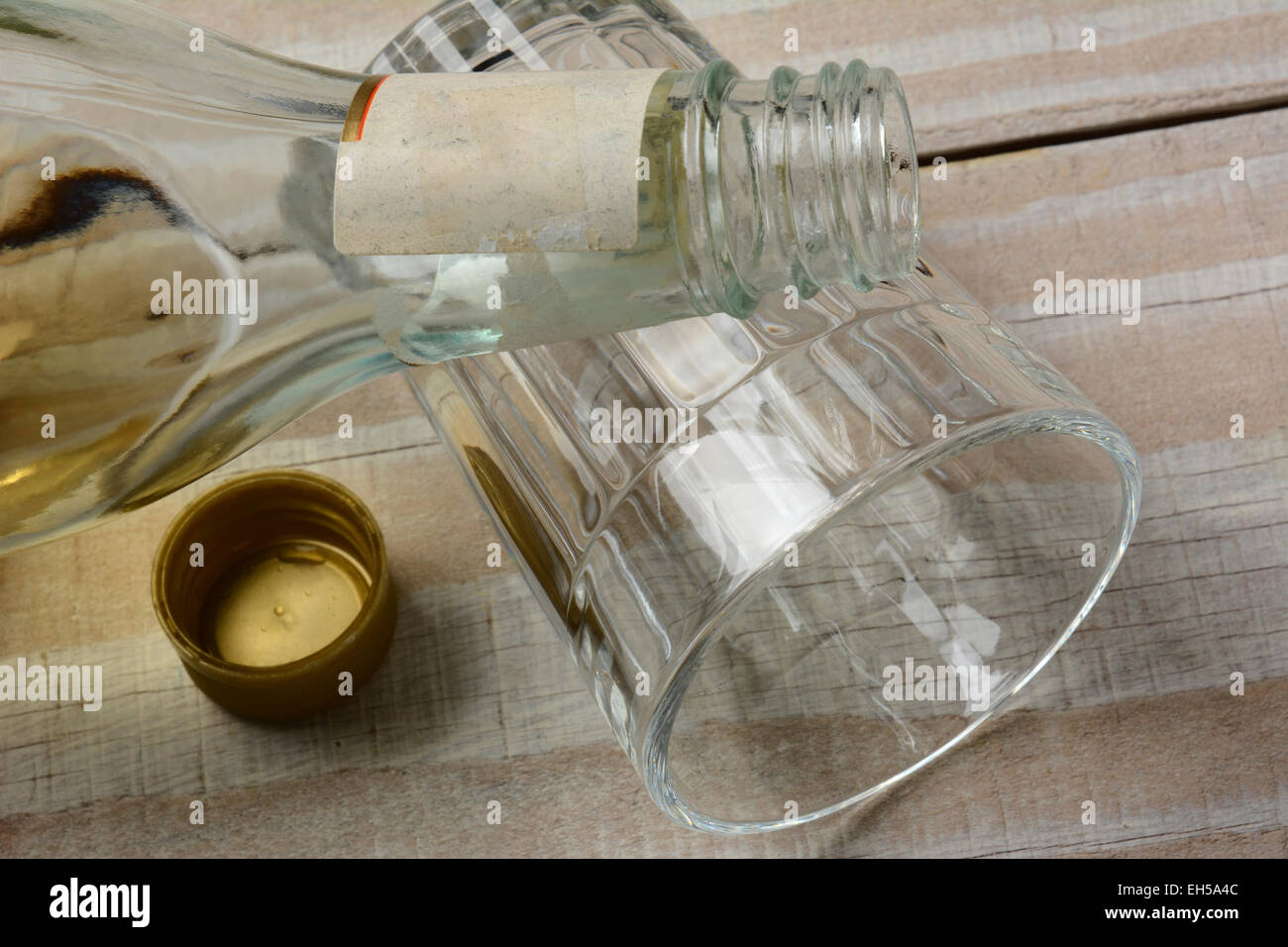 Primo piano di una bottiglia di liquore su un bicchiere vuoto recante sul suo lato. Il cappuccio è spento la bottiglia su un rustico di legno bianco tavola. Foto Stock