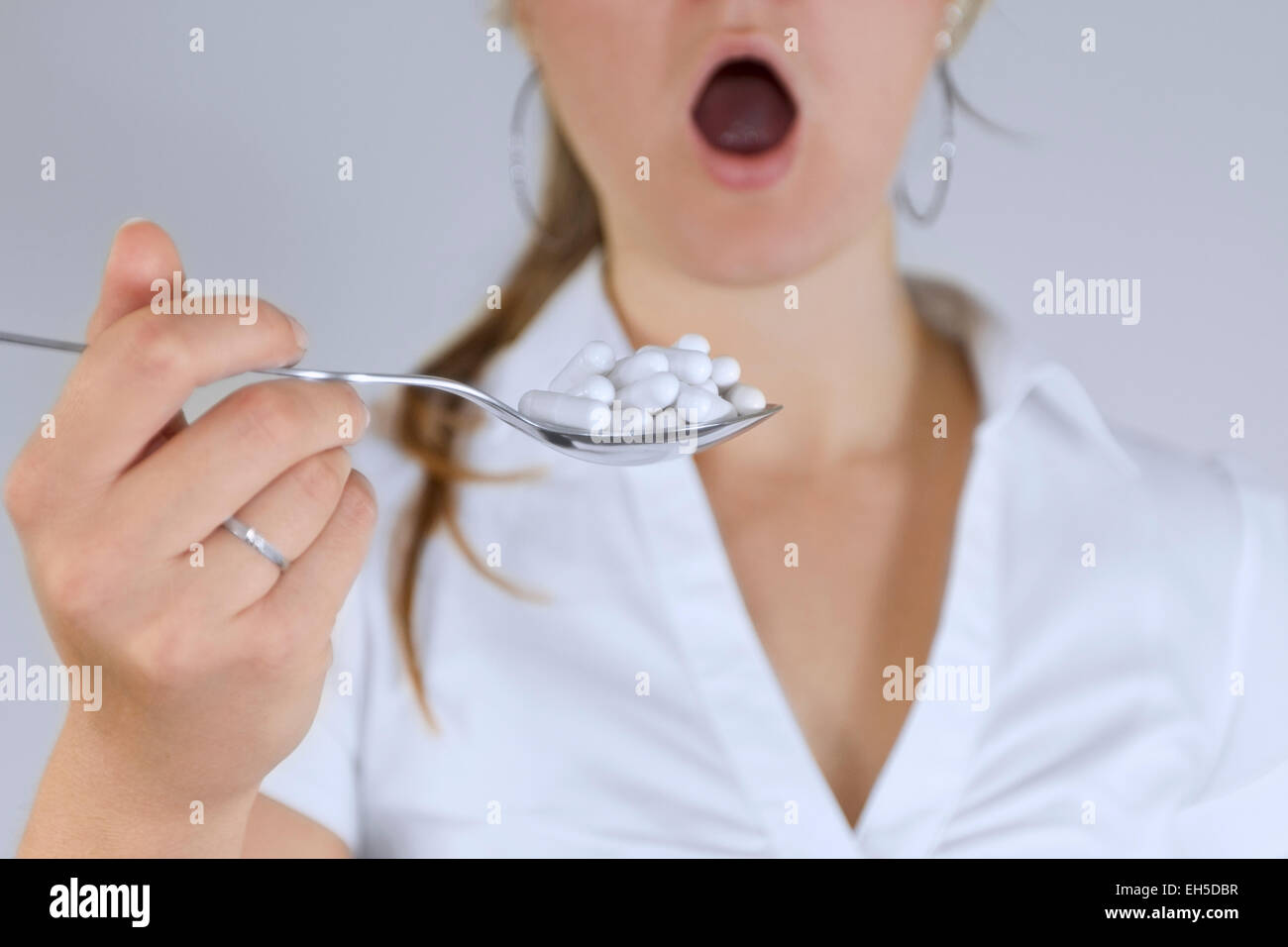 Donna con la bocca aperta prendendo un cucchiaio pieno di pillole o dando pillole. Foto Stock