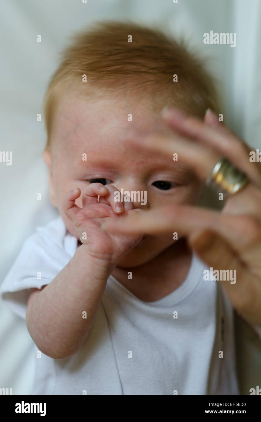 bambino di 10 settimane gioca con il dito della madre. Foto Stock
