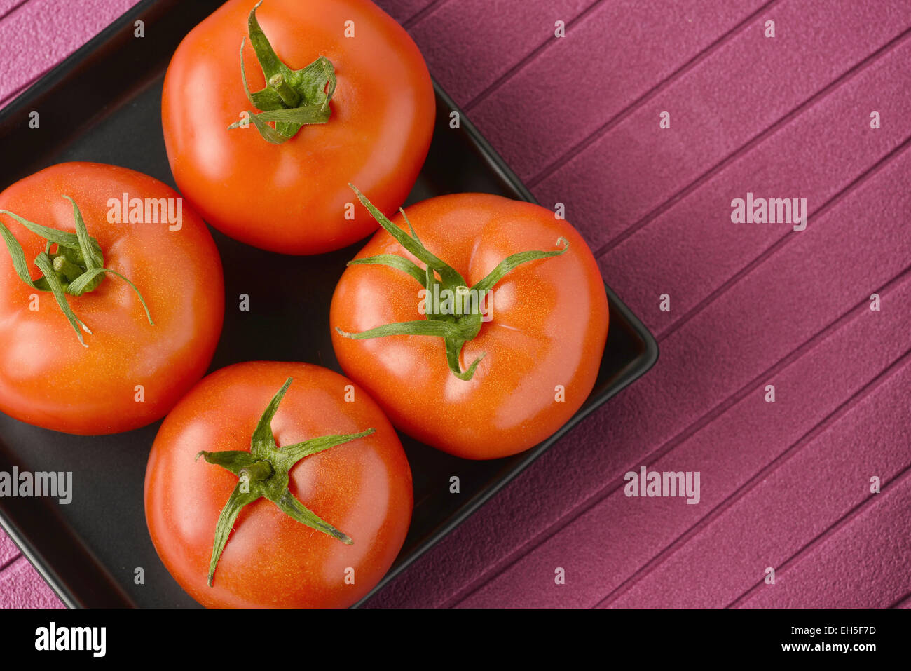 Pomodori freschi posti in un nero piastra in ceramica Foto Stock