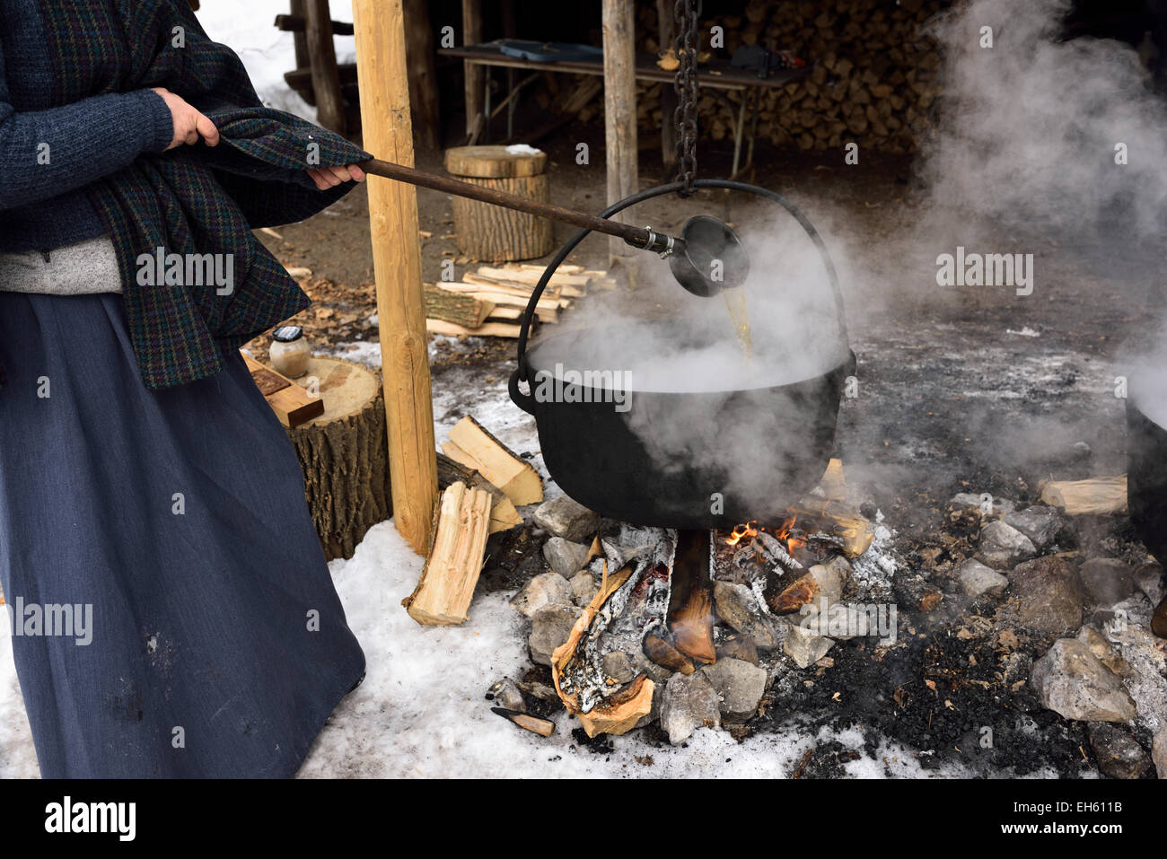 Donna in abiti da Pioneer ladling evaporando sap in ghisa pentola su fuoco di legna per la produzione di sciroppo d'acero in Ontario Canada Foto Stock