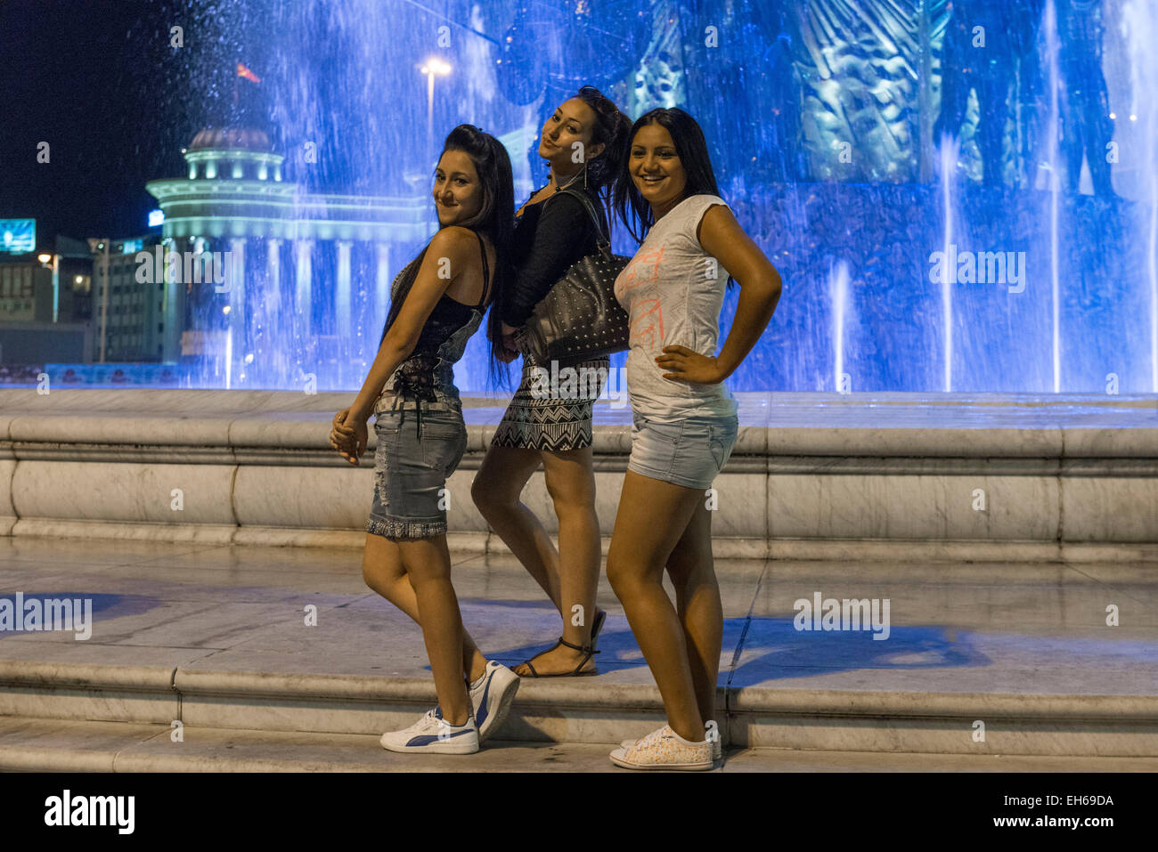 Tre ragazze in posa di notte davanti a fontana con un guerriero su un cavallo, Skopje Foto Stock