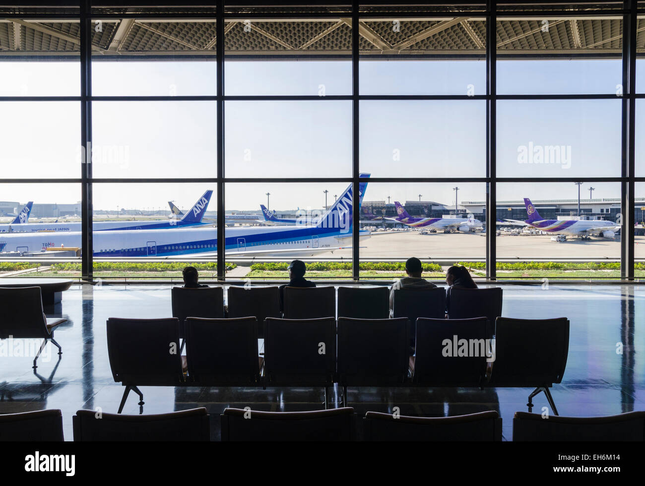 Persone sedute a Narita terminale 1, guardando attraverso le grandi finestre di vetro sopra il terminale cancelli all'Aeroporto Internazionale di Narita, Giappone Foto Stock
