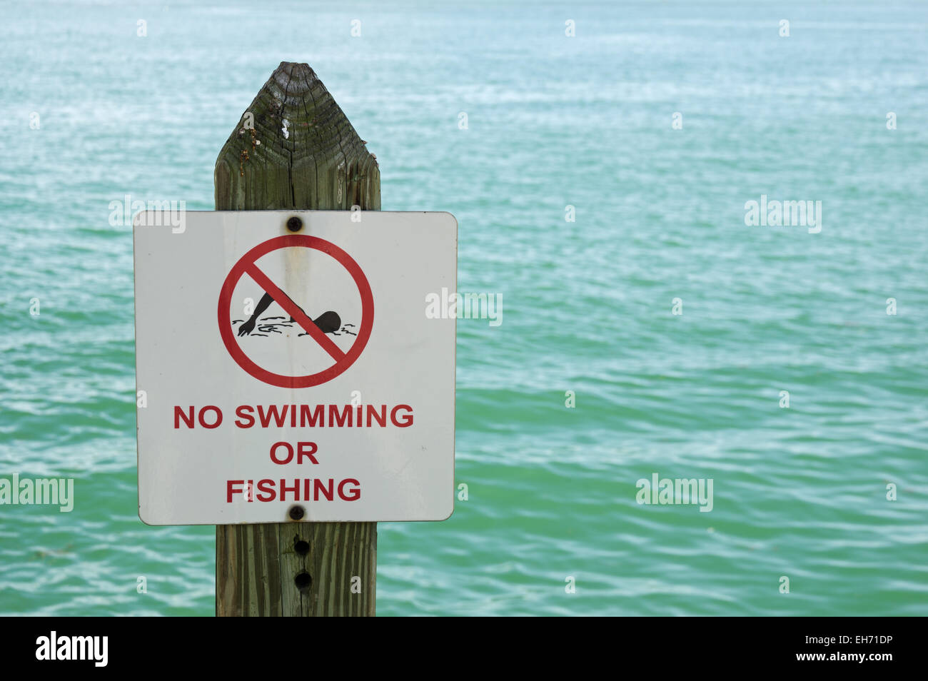 Non si può nuotare o segno di pesca su un post con fuori fuoco acqua dietro di essa Foto Stock