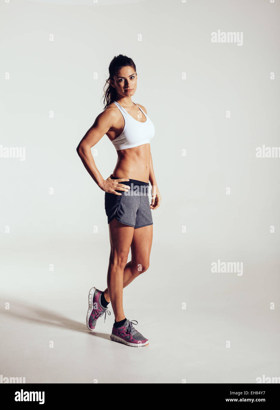 A piena lunghezza shot di giovani modello di fitness in posa di studio. Sano giovane donna abbigliamento sportivo in piedi su sfondo grigio. Foto Stock
