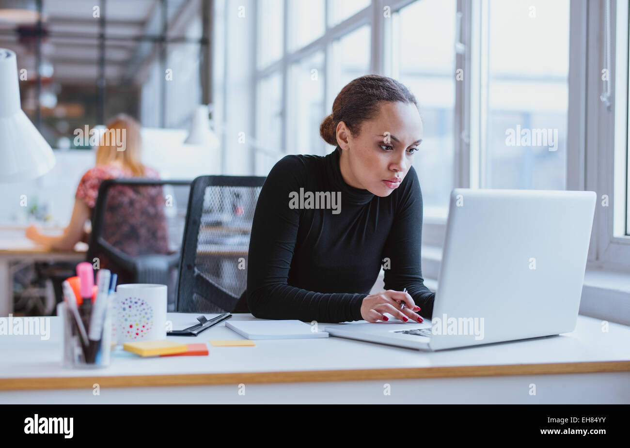 Immagine Di Donna con computer portatile mentre è seduto alla sua scrivania. Giovane americano africano imprenditrice seduta in ufficio e sul lavoro Foto Stock