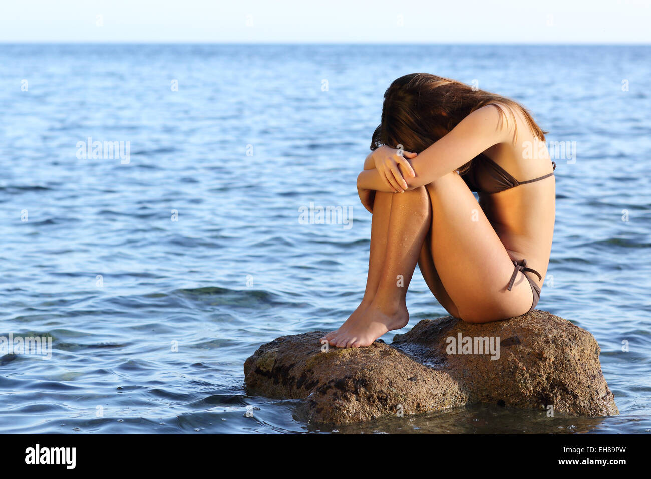 Lonely preoccupato donna seduta su una roccia sulla spiaggia nel mezzo dell'oceano Foto Stock