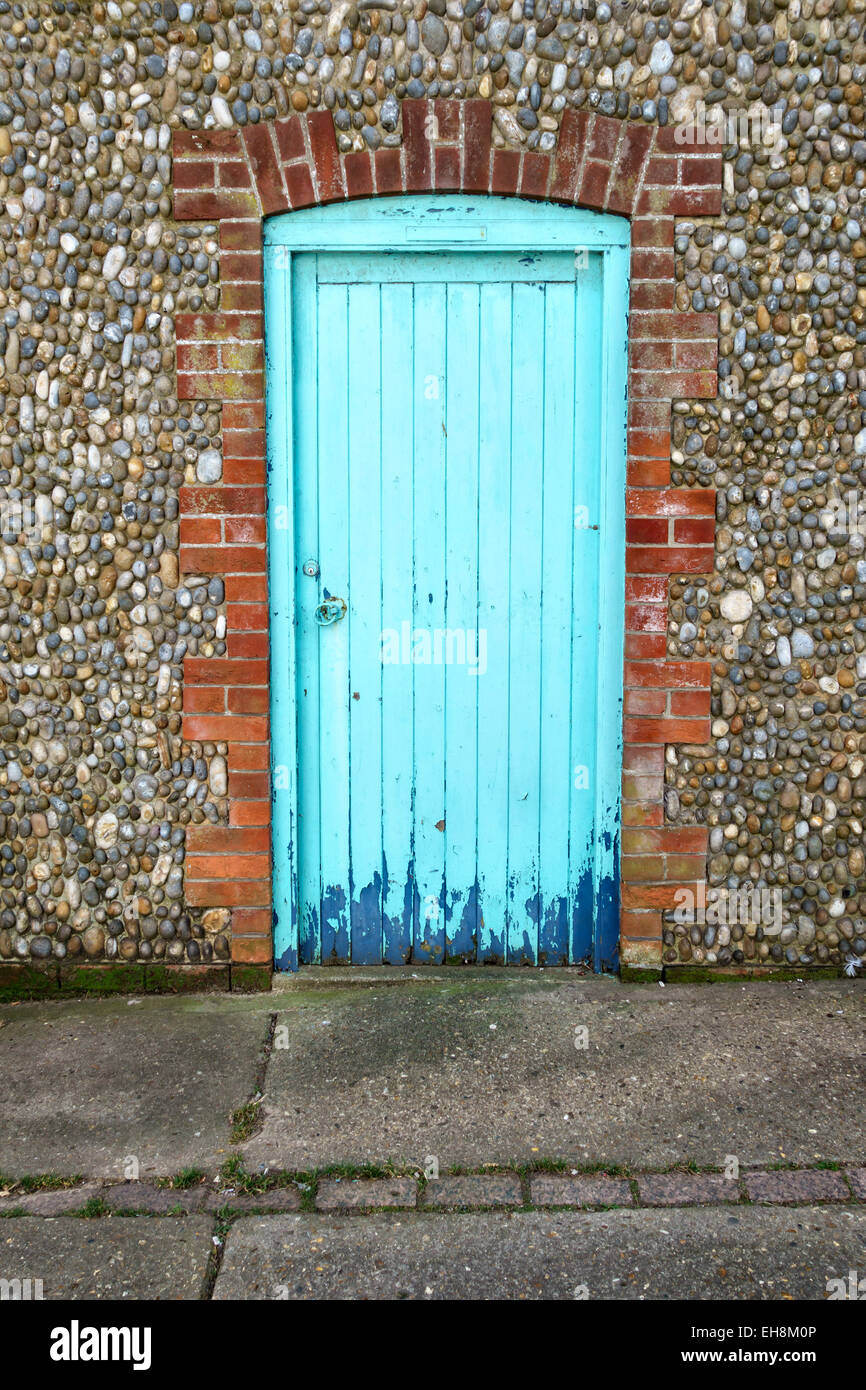 Aldeburgh, Suffolk, Regno Unito. Un blu turchese porta in un tradizionale pietra focaia di ghiaia e di un muro di mattoni Foto Stock