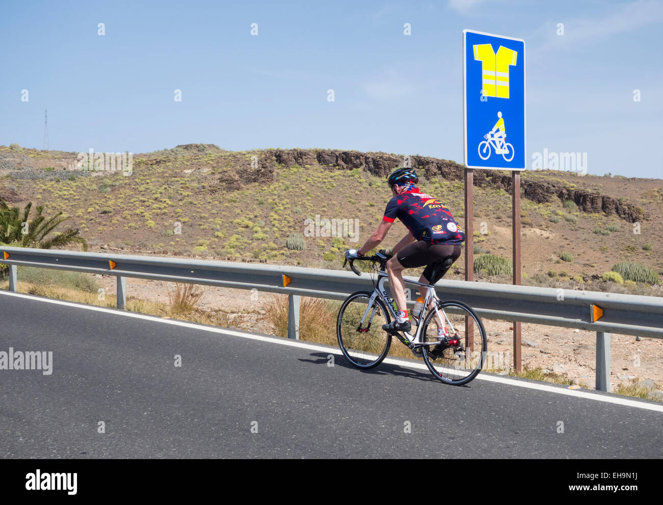 Ciclista passando segno sulla strada di montagna su Gran Canaria indicando uso obbligatorio di alta visibilità camicia Foto Stock