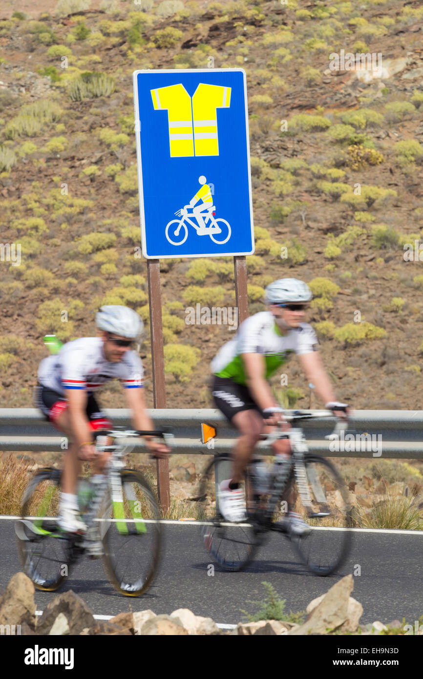 I ciclisti passando segno sulla strada di montagna su Gran Canaria indicando uso obbligatorio di alta visibilità camicia Foto Stock
