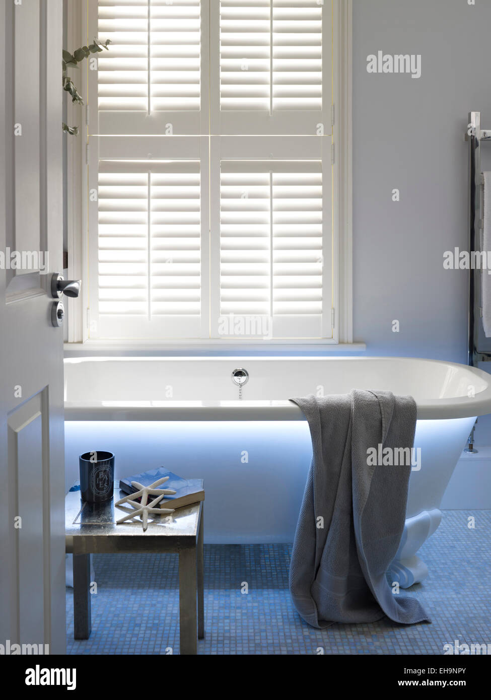 Aprire lo sportello attraverso al moderno illuminato blu vasca da bagno con asciugamani e tabella in Fernhurst Road home, REGNO UNITO Foto Stock