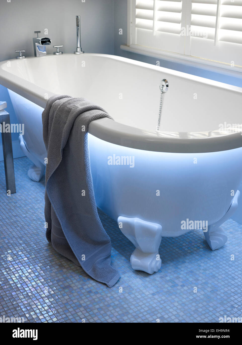 Moderno illuminato blu vasca da bagno con vasca da bagno in ceramica piedi e pavimento a mosaico dettaglio in Fernhurst Road home, REGNO UNITO Foto Stock