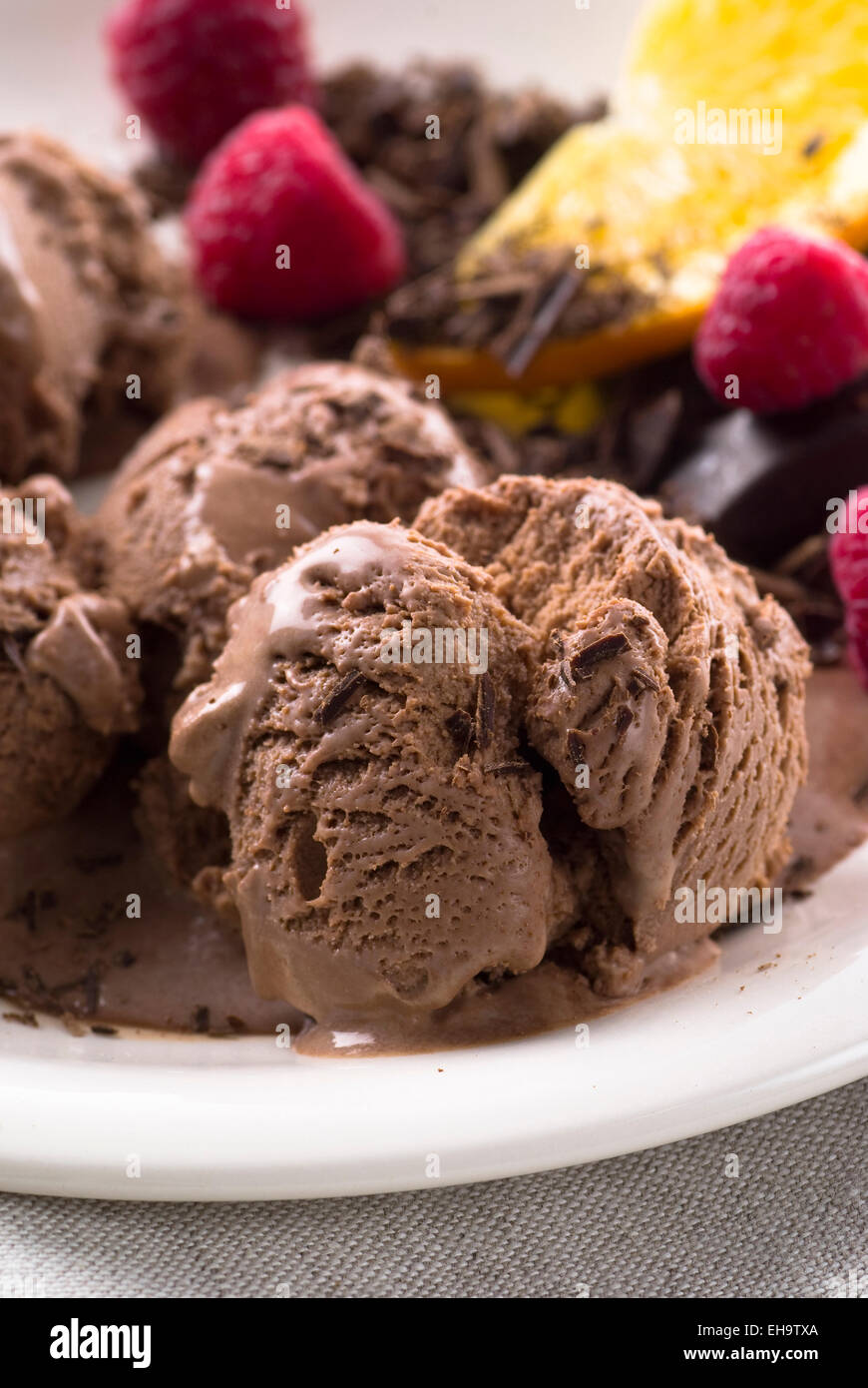 Gelato al cioccolato con cioccolato grattugiato. Lamponi freschi e fette di arancia come decorazione. Foto Stock