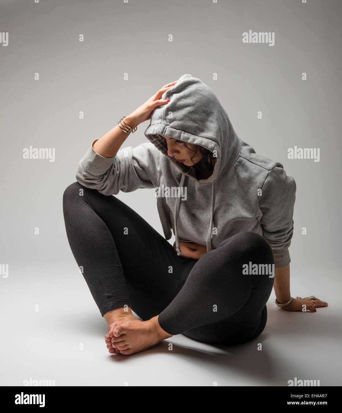 Una giovane donna adolescente ragazza introversa umore introspettivo ritirati uncommunciative, seduto sul pavimento di indossare una felpa con cappuccio grigio felpa Foto Stock