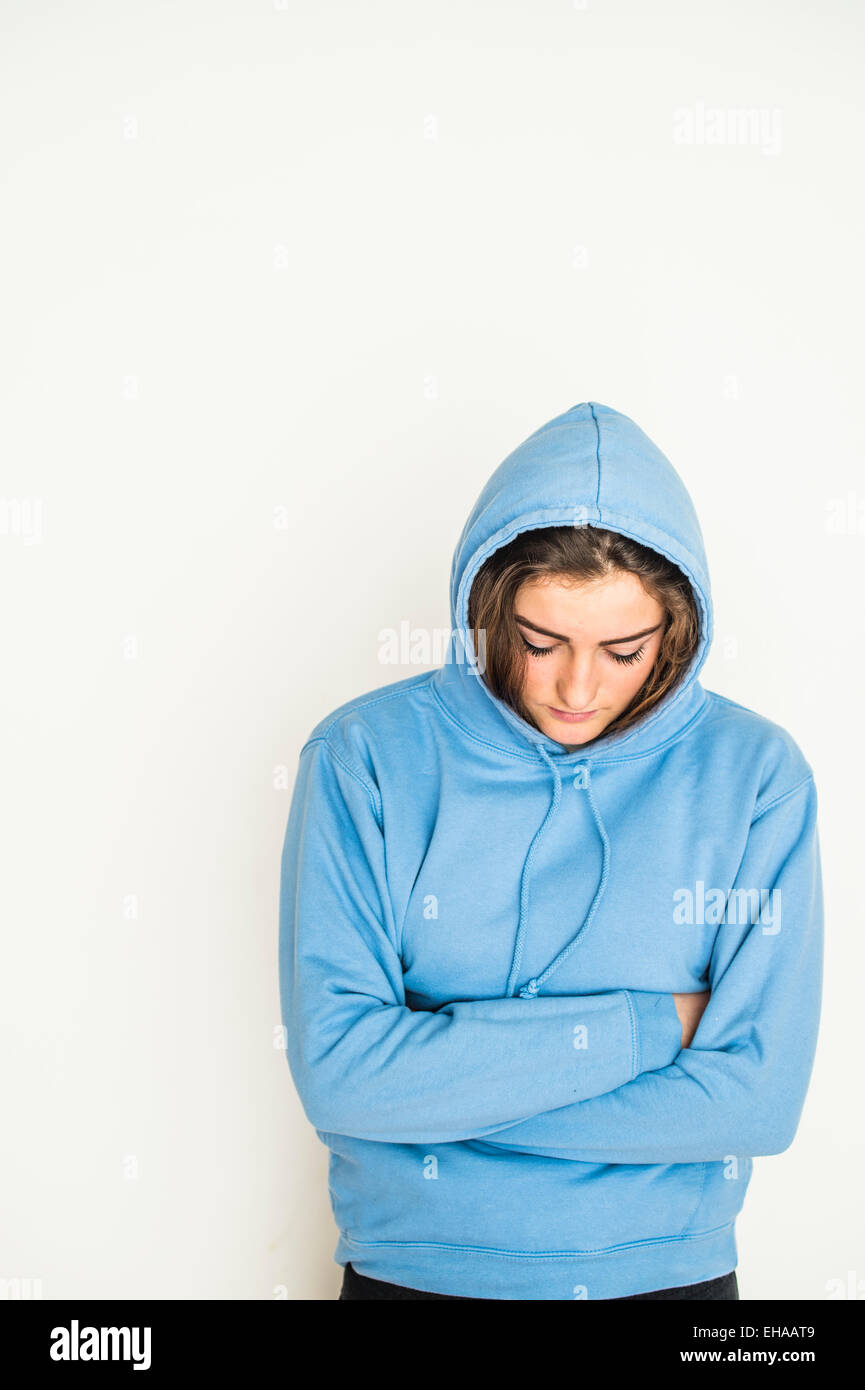 Un moody 13 14 15 anno di età giovane ragazza adolescente che indossa un blu felpa con cappuccio Felpa con cappuccio Felpa in piedi contro un bianco di sfondo per studio REGNO UNITO Foto Stock