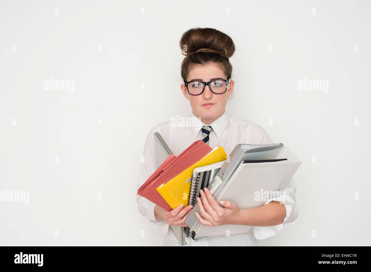 Un gravati oberati di lavoro 13 14 15 anno vecchio geek geeky da stupidi schoolgirl portando una pila di esercitare i notebook e i compiti di scuola corsi di file con gli occhiali e un'uniforme scolastica REGNO UNITO Foto Stock