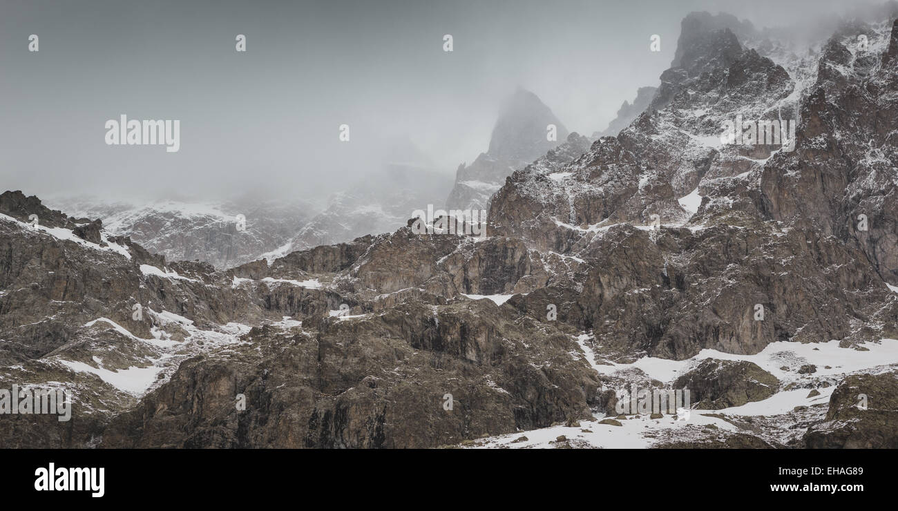 Cime frastagliate in densa nube durante una bufera di neve sulla faccia sud della Barra degli Ecrins mountain, sulle alpi francesi. Foto Stock