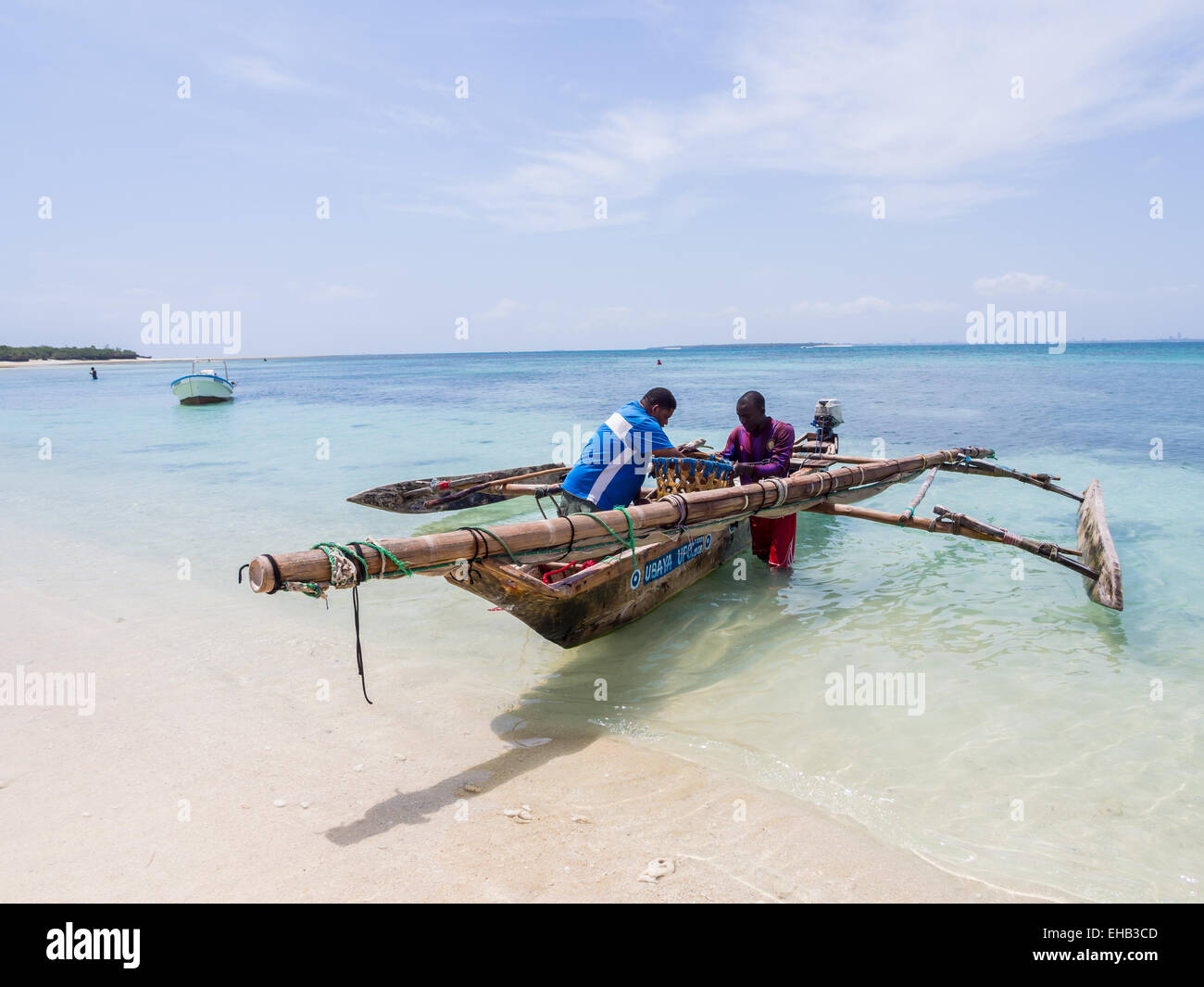 Due pescatori con una barca di legno tradizionale sulla spiaggia di Isola Mbudya in Tanzania, in Africa, in una giornata di sole. Orizzontale. Foto Stock