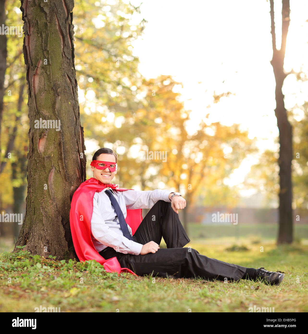 Uomo gioioso in abito di supereroi seduto in un parco shot con inclinazione e spostamento lente Foto Stock