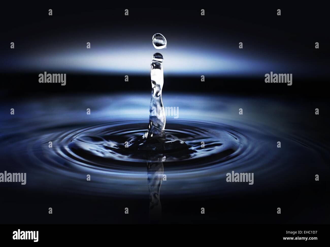 Goccia d'acqua creando onde e increspature su uno sfondo blu scuro. Foto Stock
