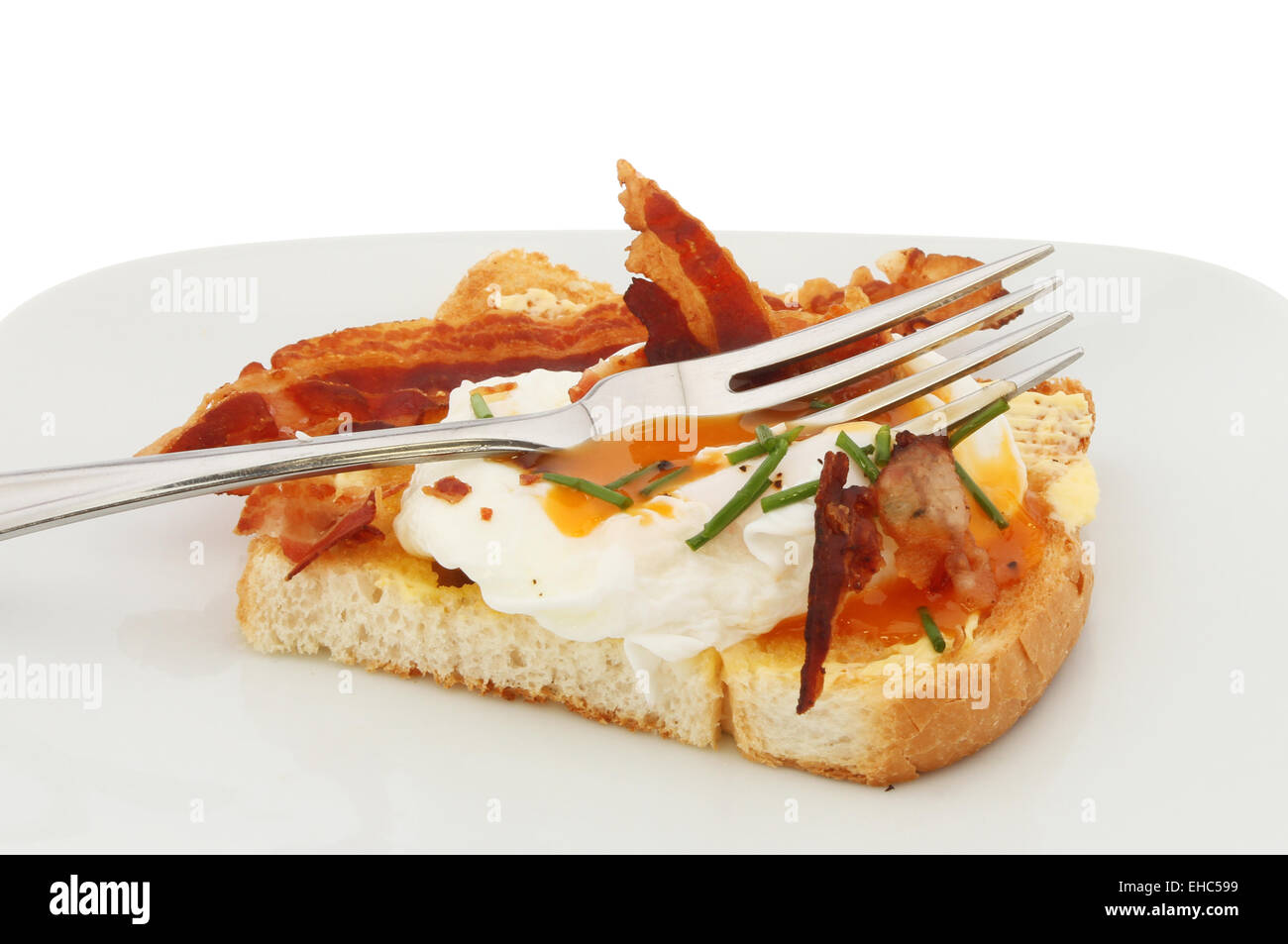 Primo piano di un uovo in camicia su toast con pancetta, erba cipollina e una forcella Foto Stock