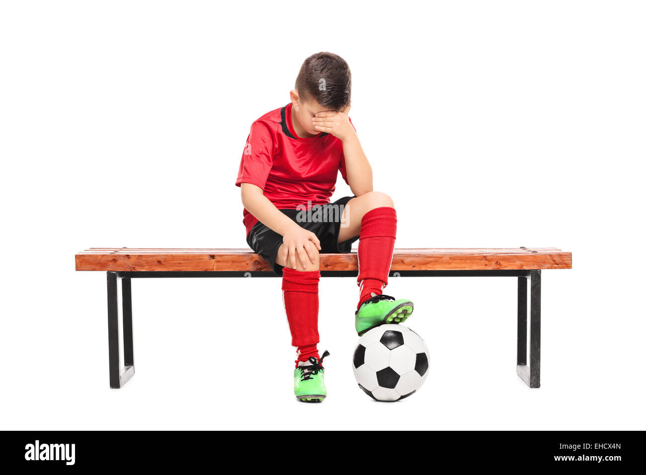 Triste kid nel calcio uniforme di seduta su una panchina isolata su sfondo bianco Foto Stock