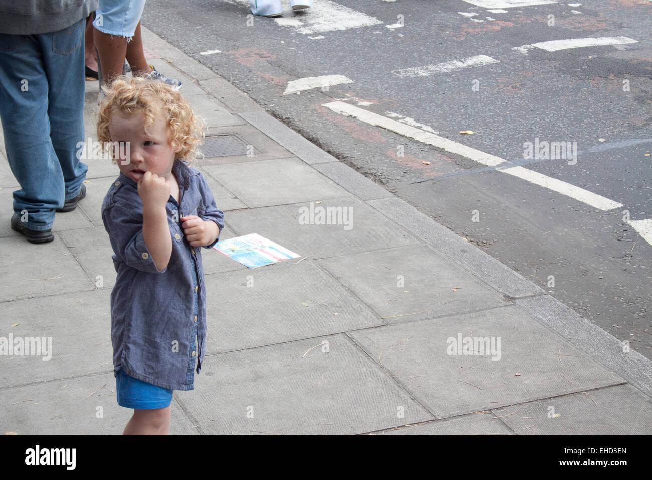 Piccolo Ragazzo (o eventualmente ragazza) da solo su un marciapiede marciapiede come Hackney Carnevale passa Foto Stock