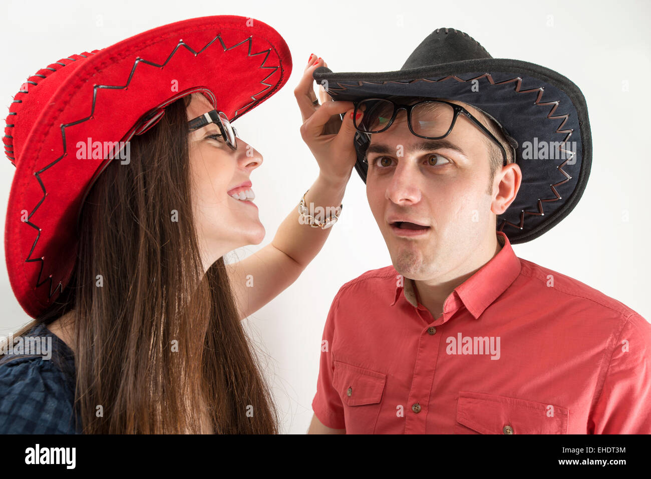 Coppia giovane con cappelli da cowboy e bicchieri rendendo silly volti su sfondo bianco Foto Stock