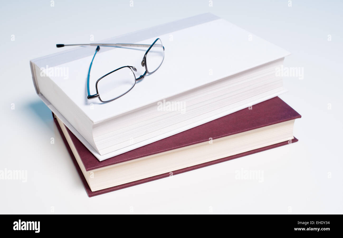 Pila di libri e un paio di occhiali per leggere su sfondo bianco Foto Stock