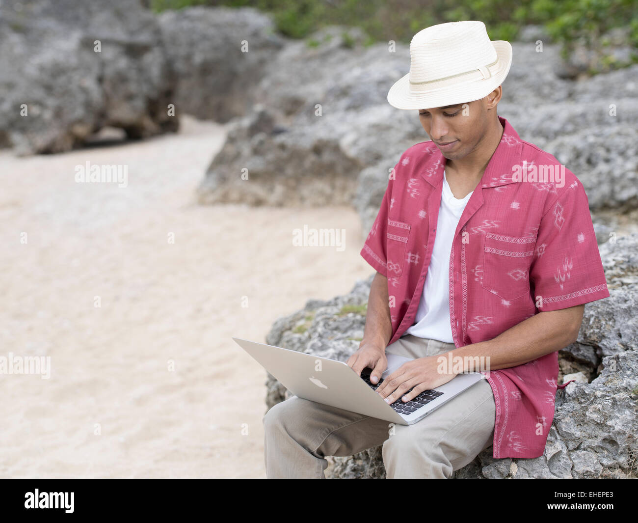 Uomo con Macbook Air di Apple computer portatile laptop al lavoro sulla spiaggia mentre è in vacanza Foto Stock