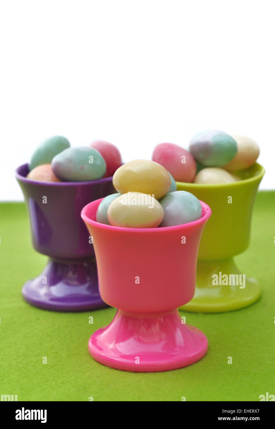 Uovo tazze riempite con piccole uova di Pasqua sul verde e Sfondo bianco Foto Stock
