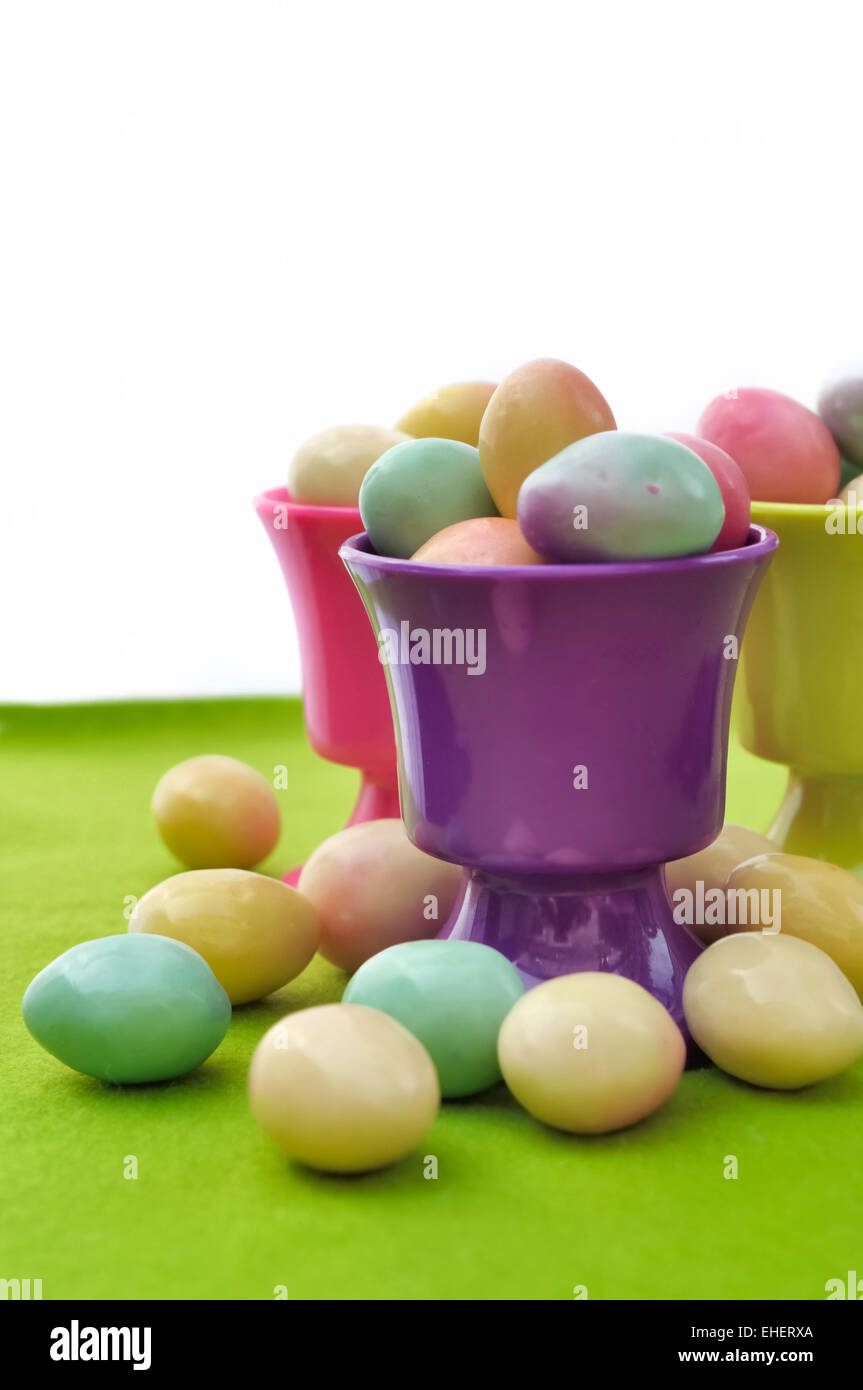 Uovo tazze riempite con piccole uova di Pasqua sul verde e Sfondo bianco Foto Stock