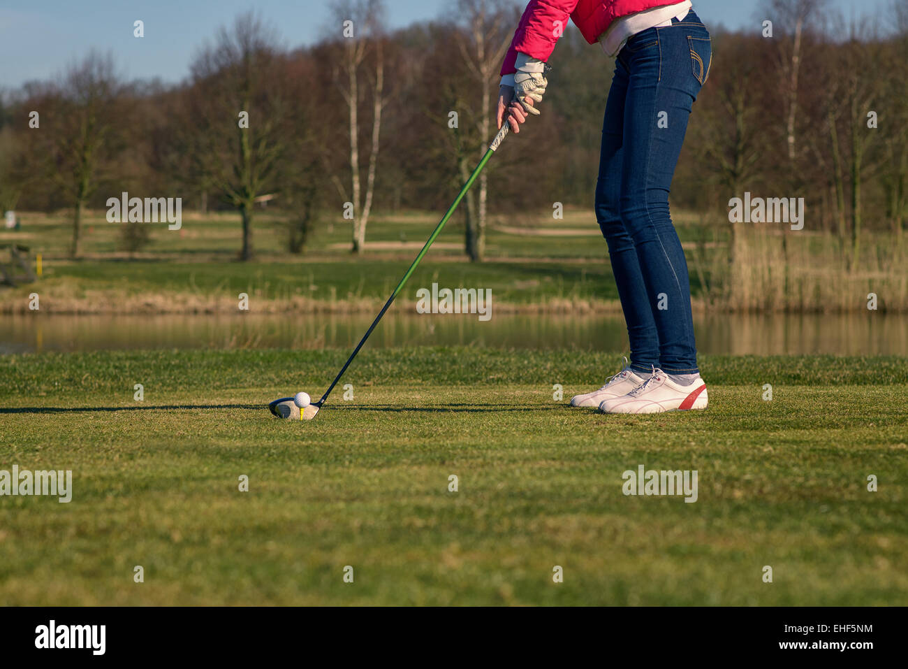 Donna di rinvio su un campo da golf in piedi nella scatola a t di fronte a un pericolo in acqua con un autista nelle sue mani pronto a tee-off Foto Stock