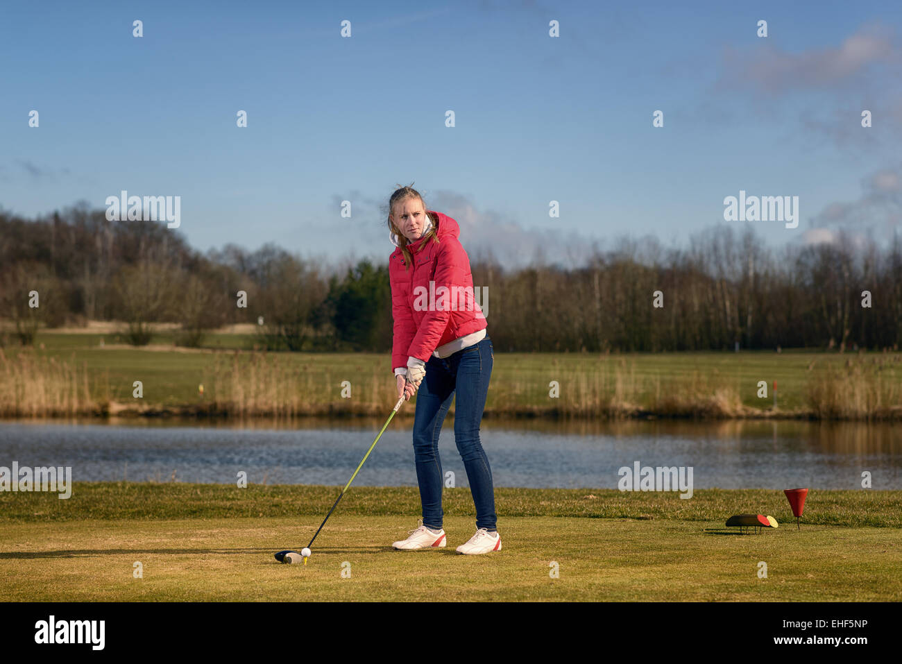 Donna di rinvio su un campo da golf in piedi nella scatola a t di fronte a un pericolo in acqua con un autista nelle sue mani pronto a tee-off Foto Stock