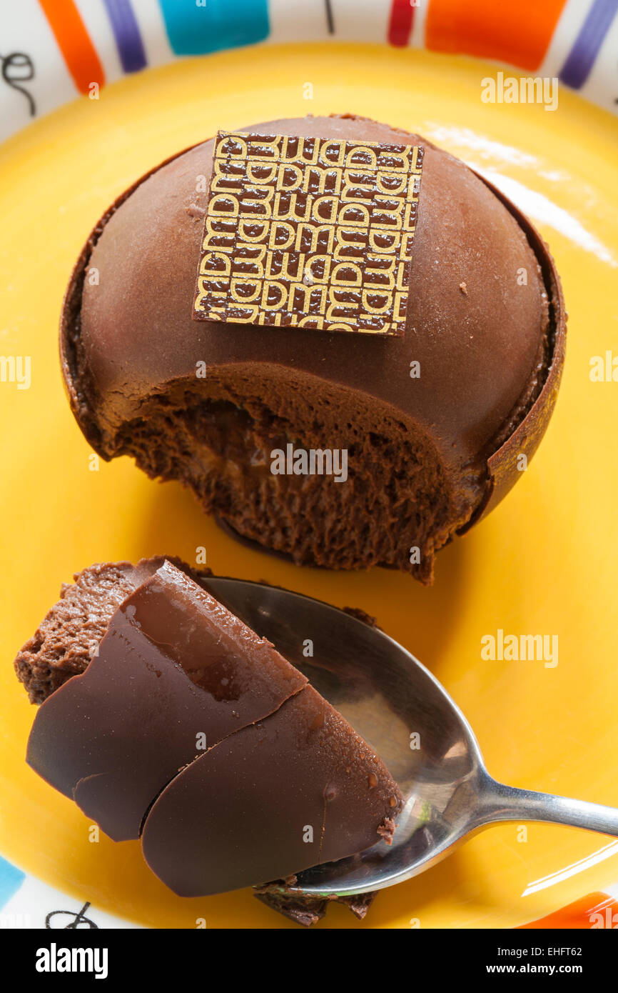 Prendere una cucchiaiata di Marks & Spencer Cioccolato Belga Jaffa sfere dalla loro Dessert Menu impostato su colorato piastra giallo Foto Stock